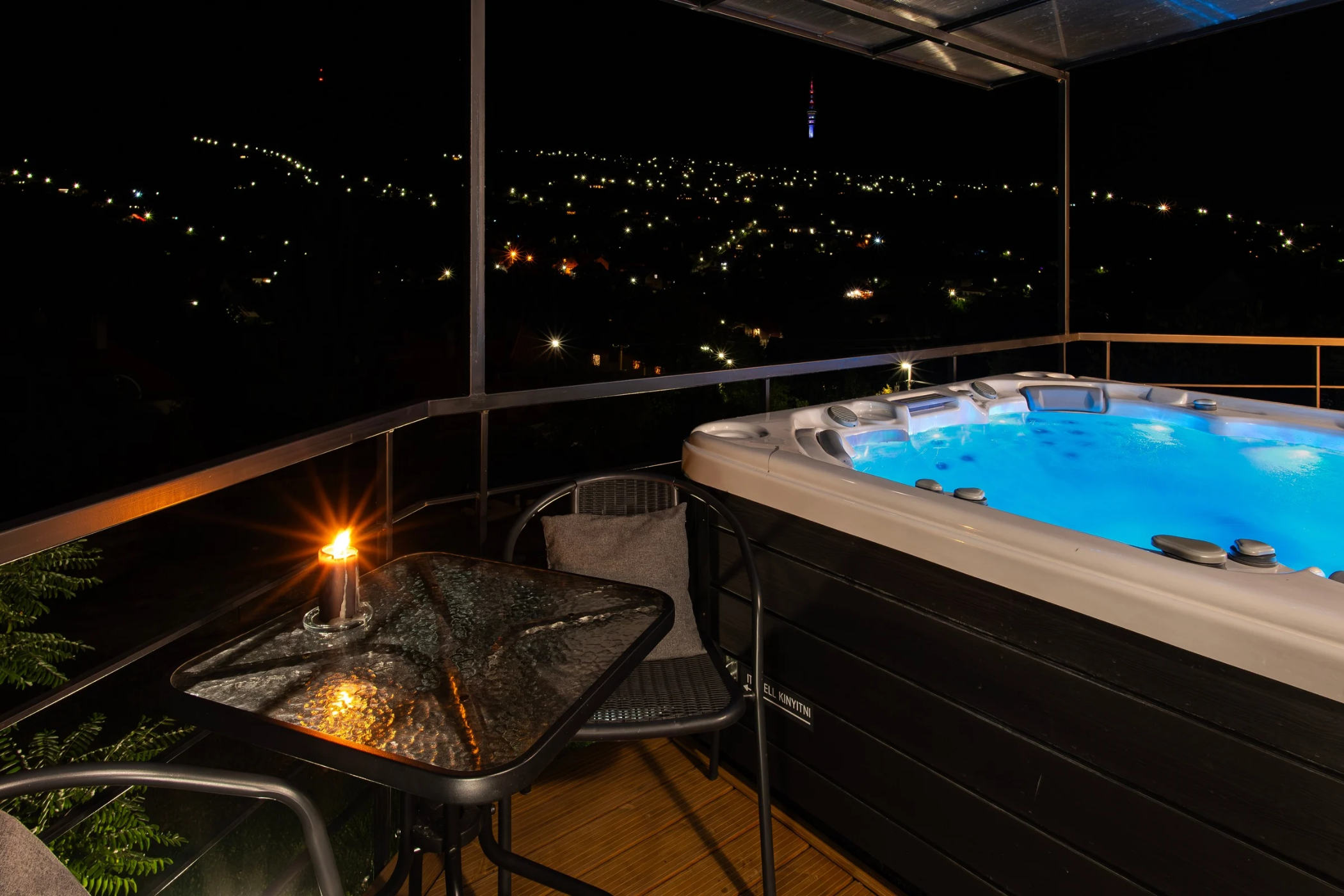 Privát jakuzzi a teraszon este, háttérben a városi panorámával.